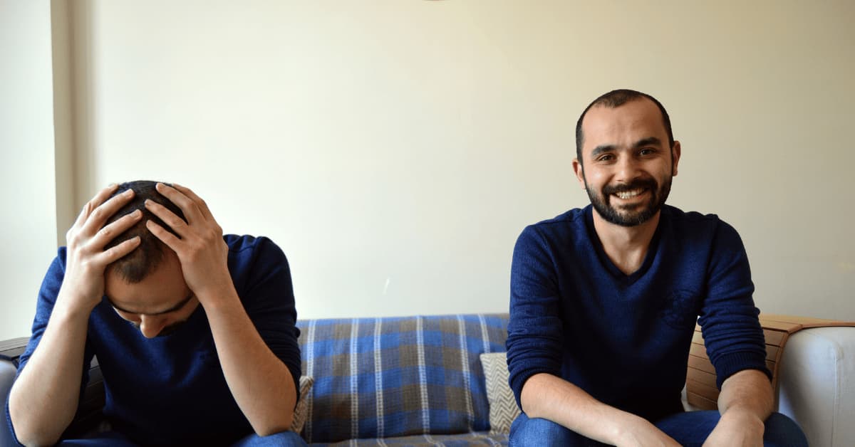 Two men sitting together on a couch, one appearing happy while the other shows signs of distress, illustrating how people can experience depression even when others seem unaware.