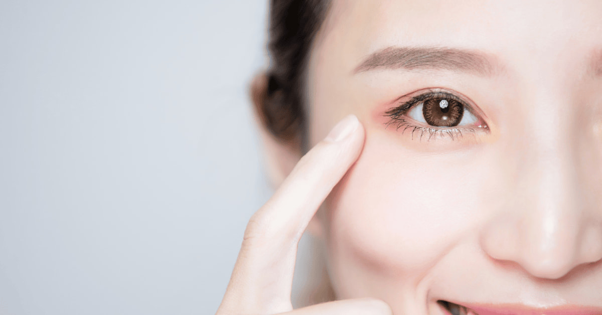 Close-up of a woman gently touching the area near her eye to show eye health and dryness symptoms.