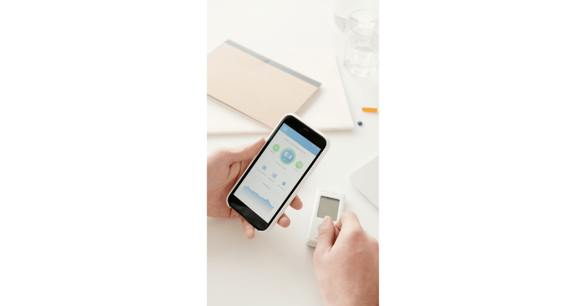 Person using a smartphone app for diabetes alongside a glucometer to track blood sugar levels at home.