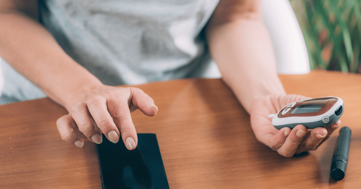 Person using a glucometer and smartphone app for diabetes to check and record blood sugar levels.