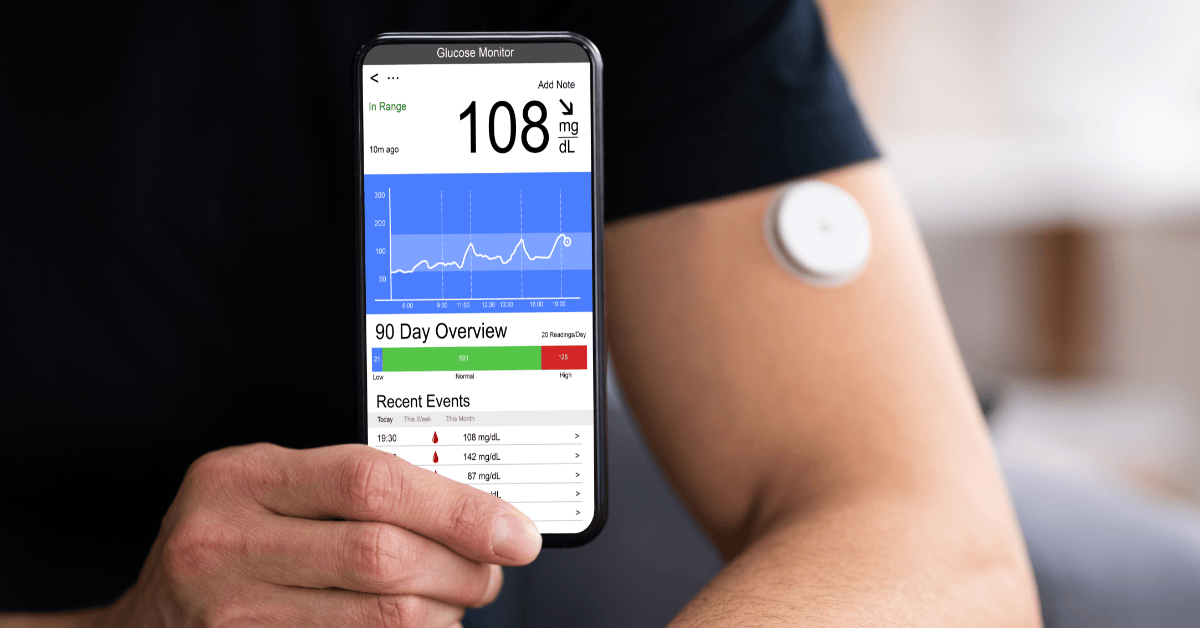 Person using a smartphone app for diabetes to monitor blood sugar levels alongside a wearable glucose sensor on their arm.
