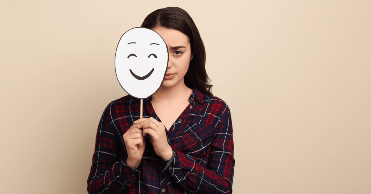 Woman holding a sad face mask symbolizing hidden mental illness and emotional struggles across all ages